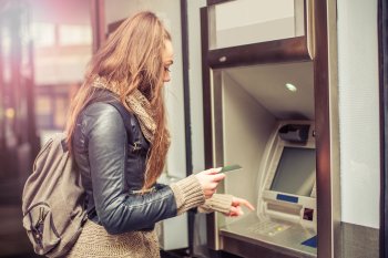 Studentin steht mit ihrer Bankkarte in der Hand am Bankautomaten